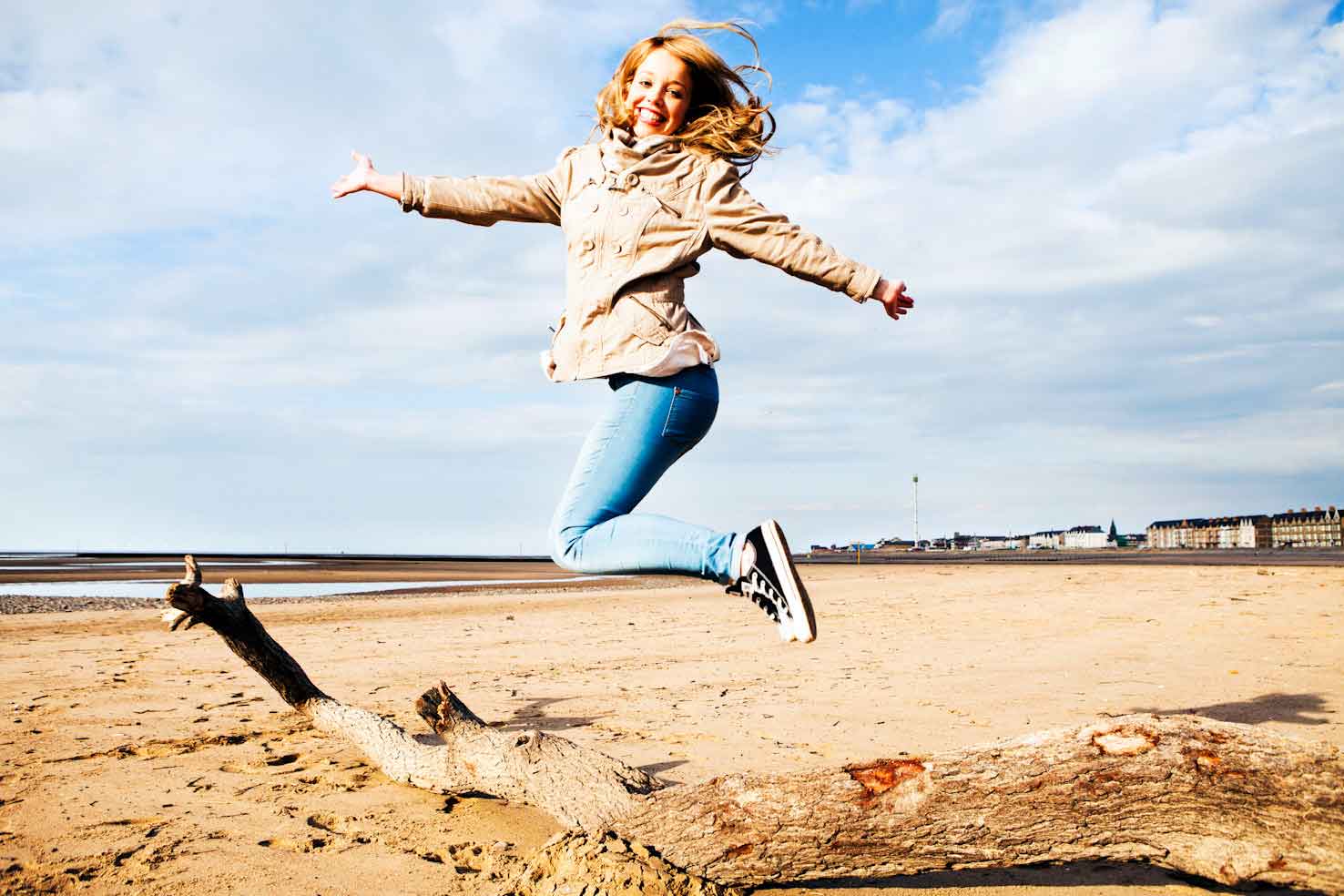Woman leaping over a tree branch on beach in Rhyl